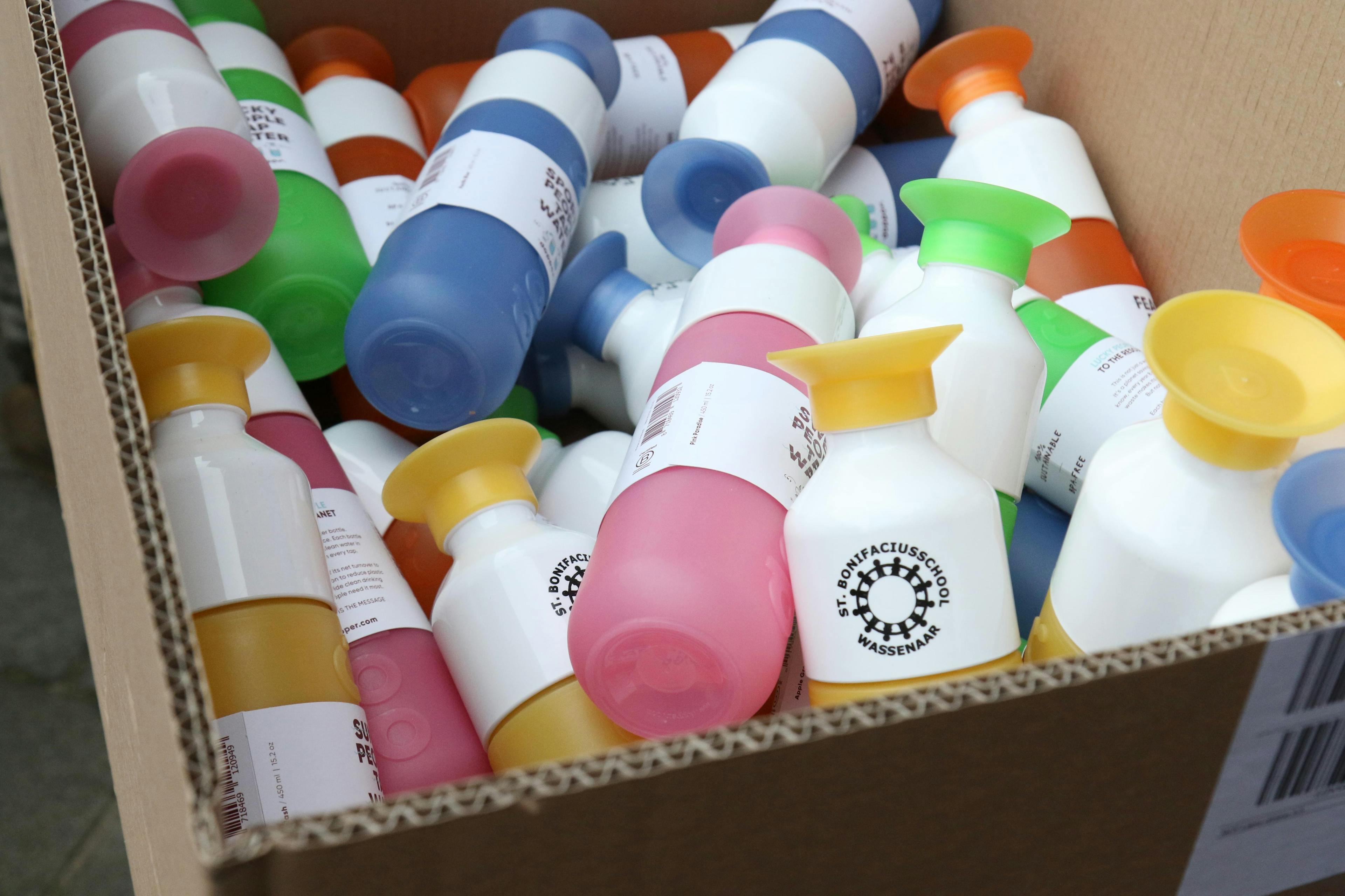 A box filled with colourful Dopper bottles and a school's logo on the cups