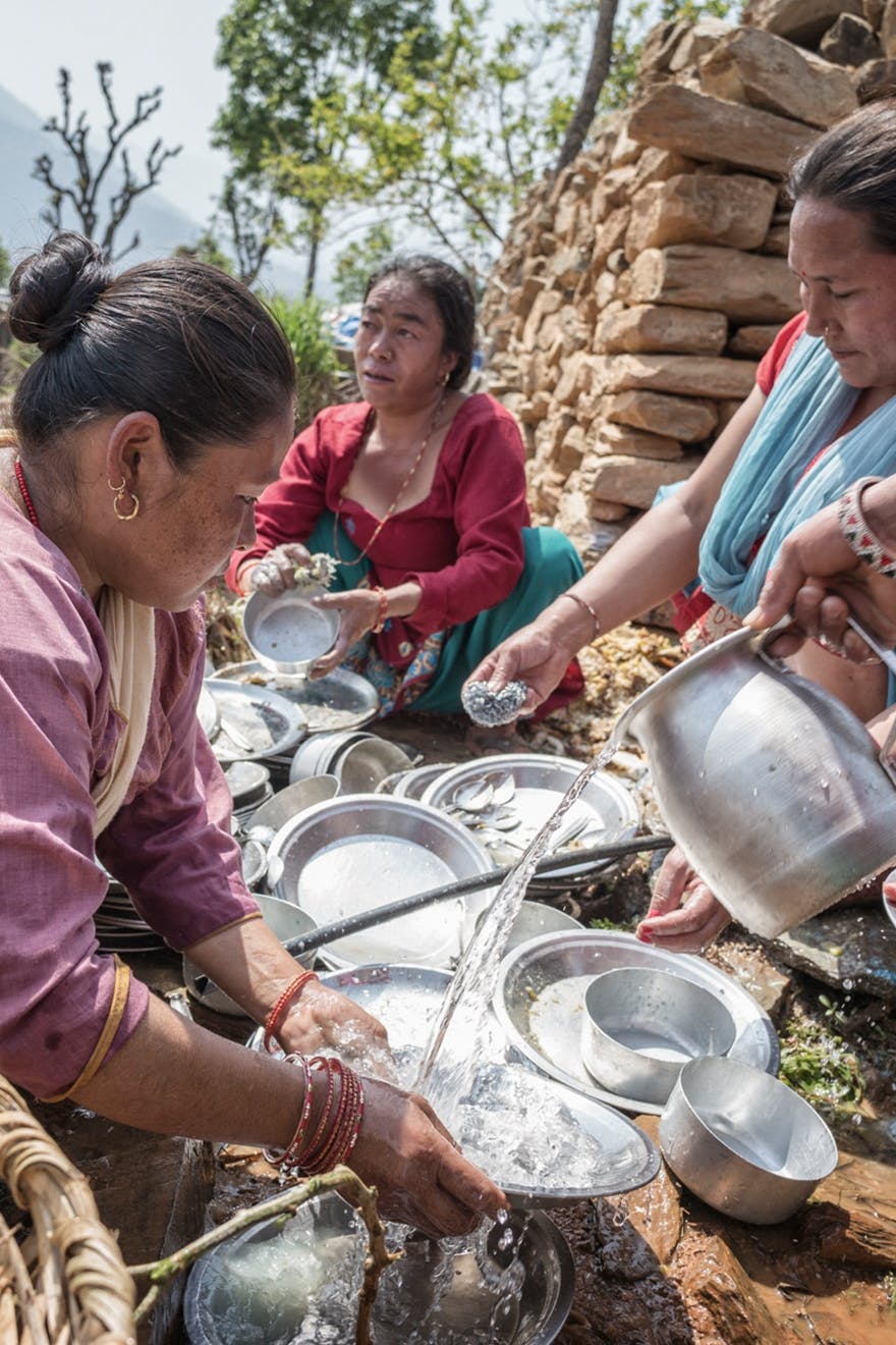 Three Nepal women cleaning dishes with water
